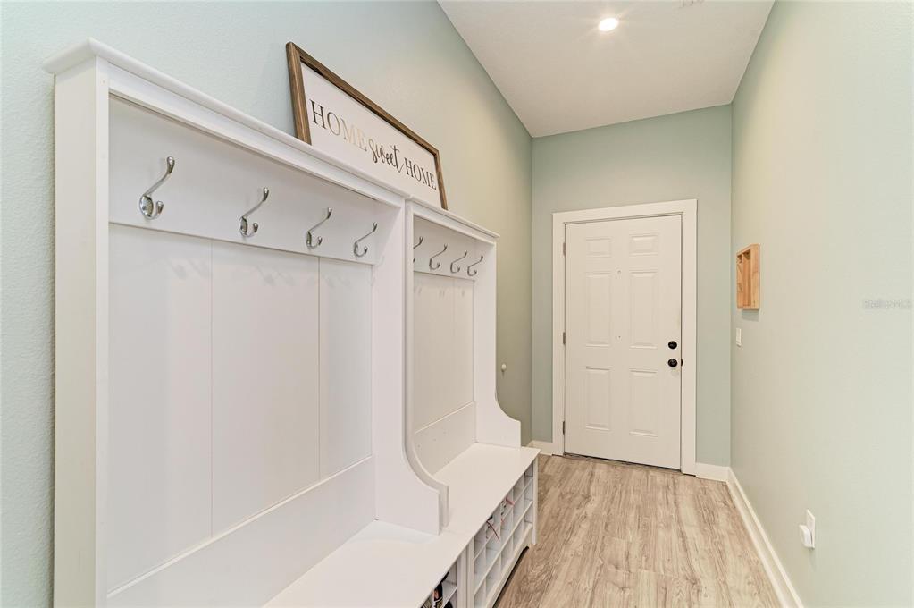 A mudroom features a white built-in storage bench with hooks and light-colored wood flooring — 1609 17TH STREET W, BRADENTON, FL