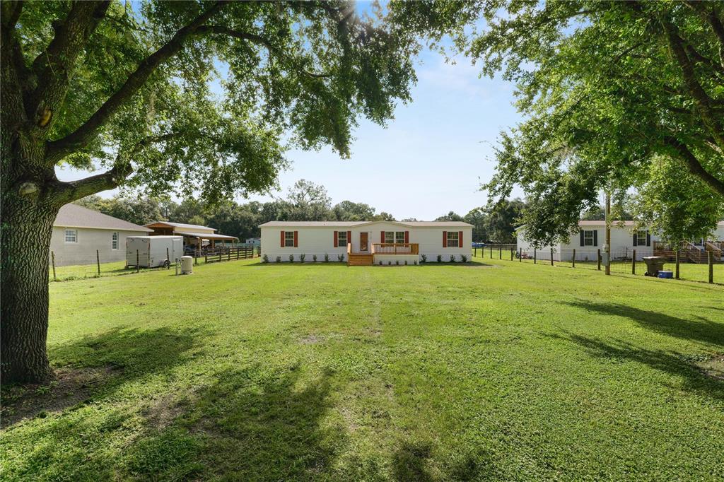 A single-story manufactured home sits in the center of a large, grassy, tree-lined yard — 7103 GLEN MEADOW DRIVE, LAKELAND, FL