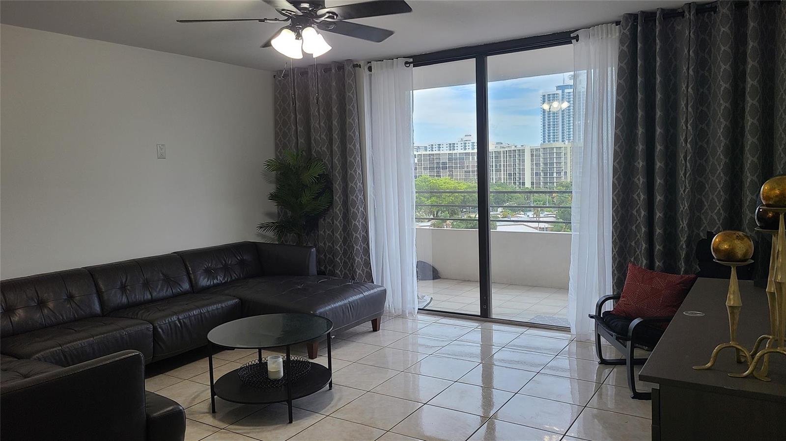 A living room with a dark leather sectional, tile flooring, and a sliding door to a balcony — 2500 Parkview Drive # 802, Hallandale Beach FL 33009, HALLANDALE BEACH, FL