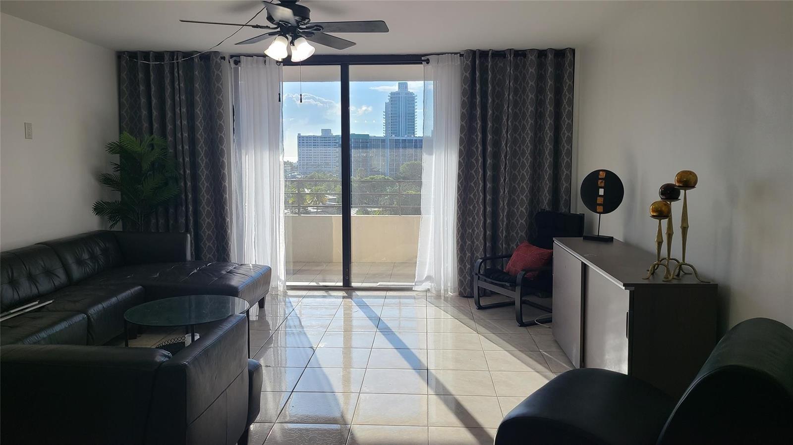 A living room with a black leather sectional, tile floors, and a balcony with city views — 2500 Parkview Drive # 802, Hallandale Beach FL 33009, HALLANDALE BEACH, FL