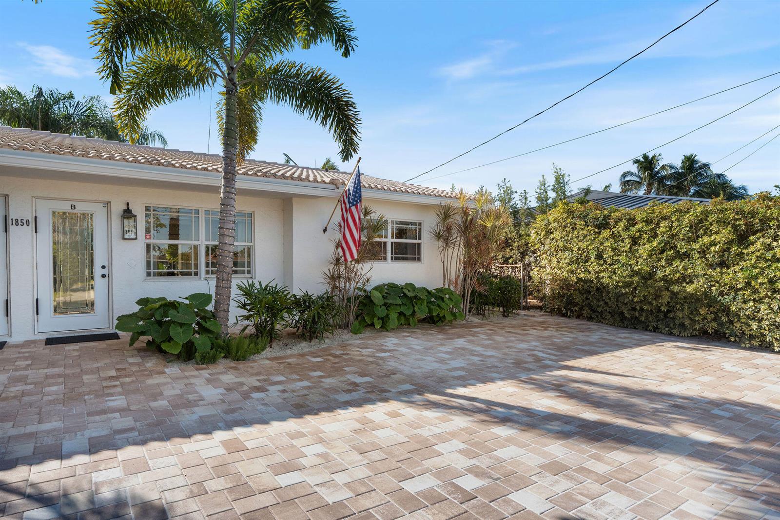 A white house exterior features a paved driveway, a palm tree, and an American flag — 1850 SE 7th Street # B, Pompano Beach FL 33060, POMPANO BEACH, FL