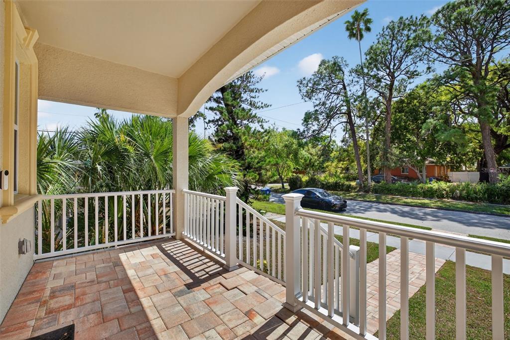 A covered porch with paver flooring and white railings overlooks a street with trees — 711 28TH AVENUE S, ST PETERSBURG, FL