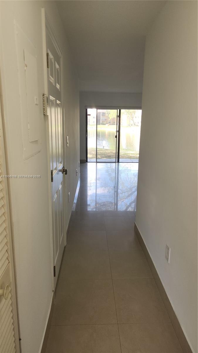 A narrow hallway with light-colored tile flooring leads toward a sliding glass door overlooking water — 210 E Palm Cir E, Pembroke Pines FL 33025, PEMBROKE PINES, FL