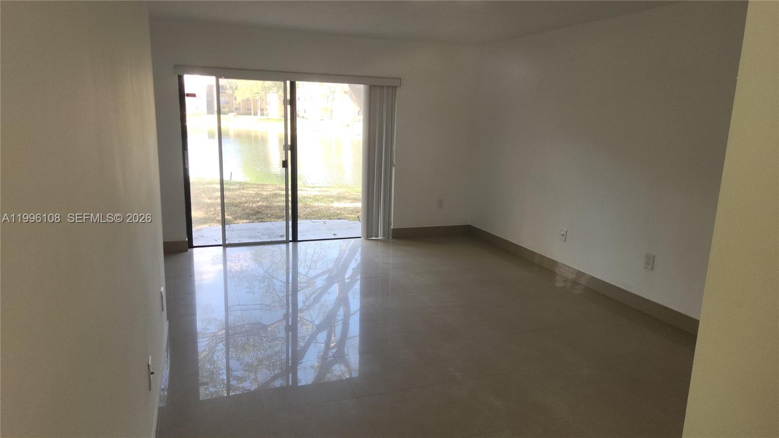 An empty room features light-colored tile flooring, white walls, and a sliding glass door — 210 E Palm Cir E, Pembroke Pines FL 33025, PEMBROKE PINES, FL