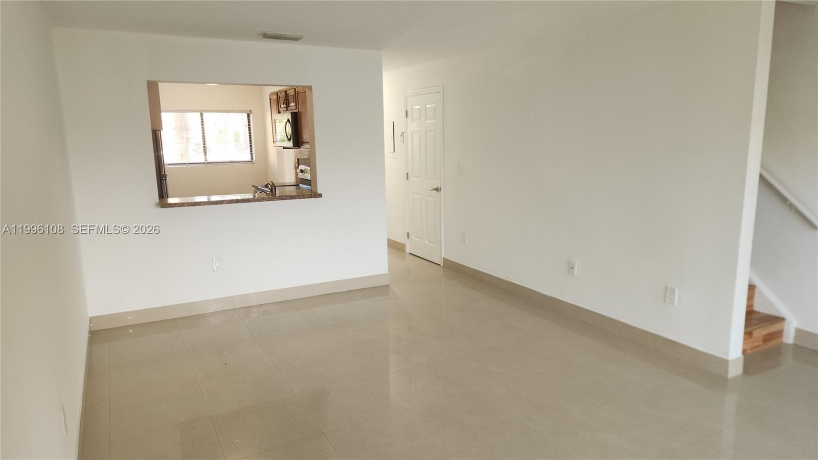 An empty room with light tile flooring, a kitchen pass-through window, and a staircase — 210 E Palm Cir E, Pembroke Pines FL 33025, PEMBROKE PINES, FL