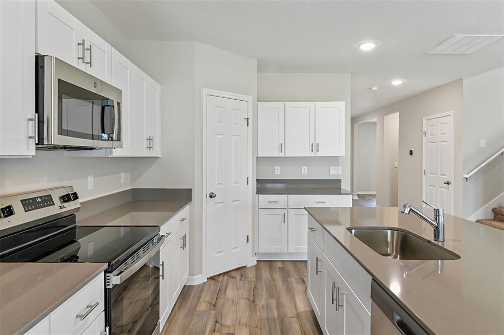 A kitchen features white cabinets, stainless steel appliances, gray countertops, and wood-look flooring — 4385 PRAIRIE RUN, HAINES CITY, FL