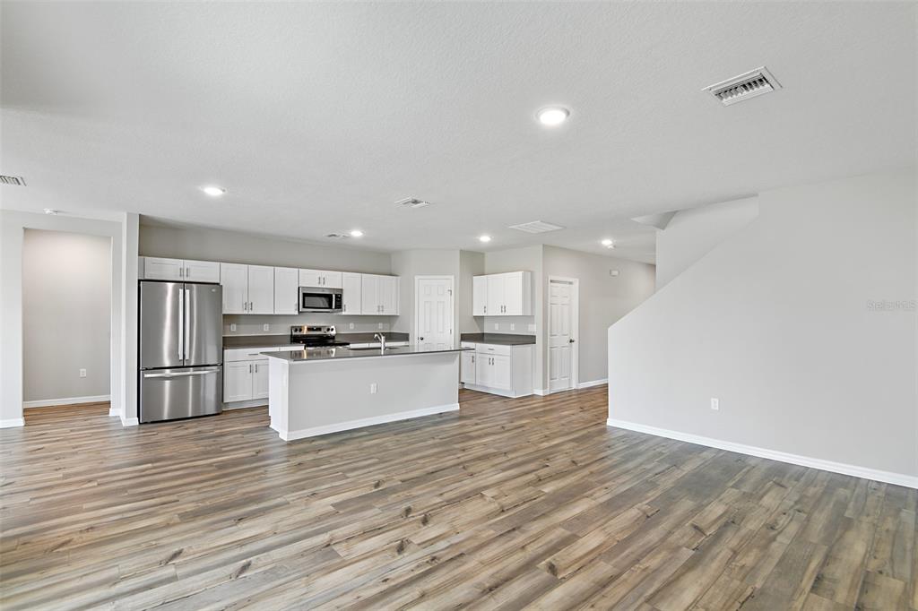 A modern kitchen with white cabinets, stainless steel appliances, and wood-look flooring — 4385 PRAIRIE RUN, HAINES CITY, FL