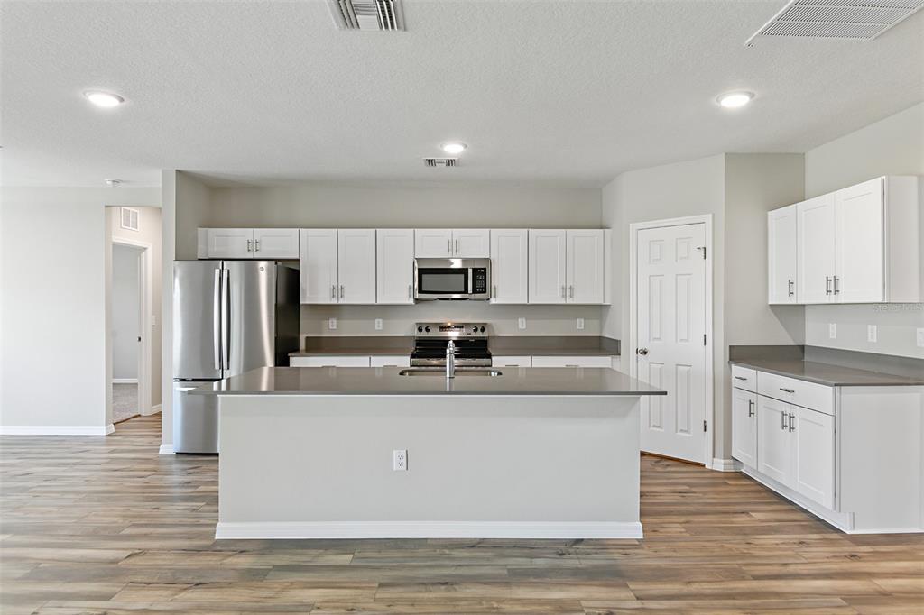 A modern kitchen features white cabinets, stainless steel appliances, a center island, and wood-look flooring — 4385 PRAIRIE RUN, HAINES CITY, FL
