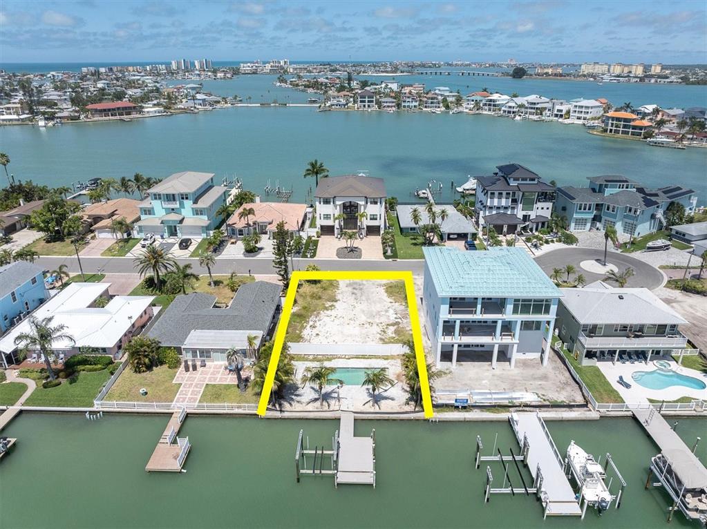 An aerial view shows a vacant waterfront lot with a pool and dock between two houses — 575 CRYSTAL DRIVE, MADEIRA BEACH, FL