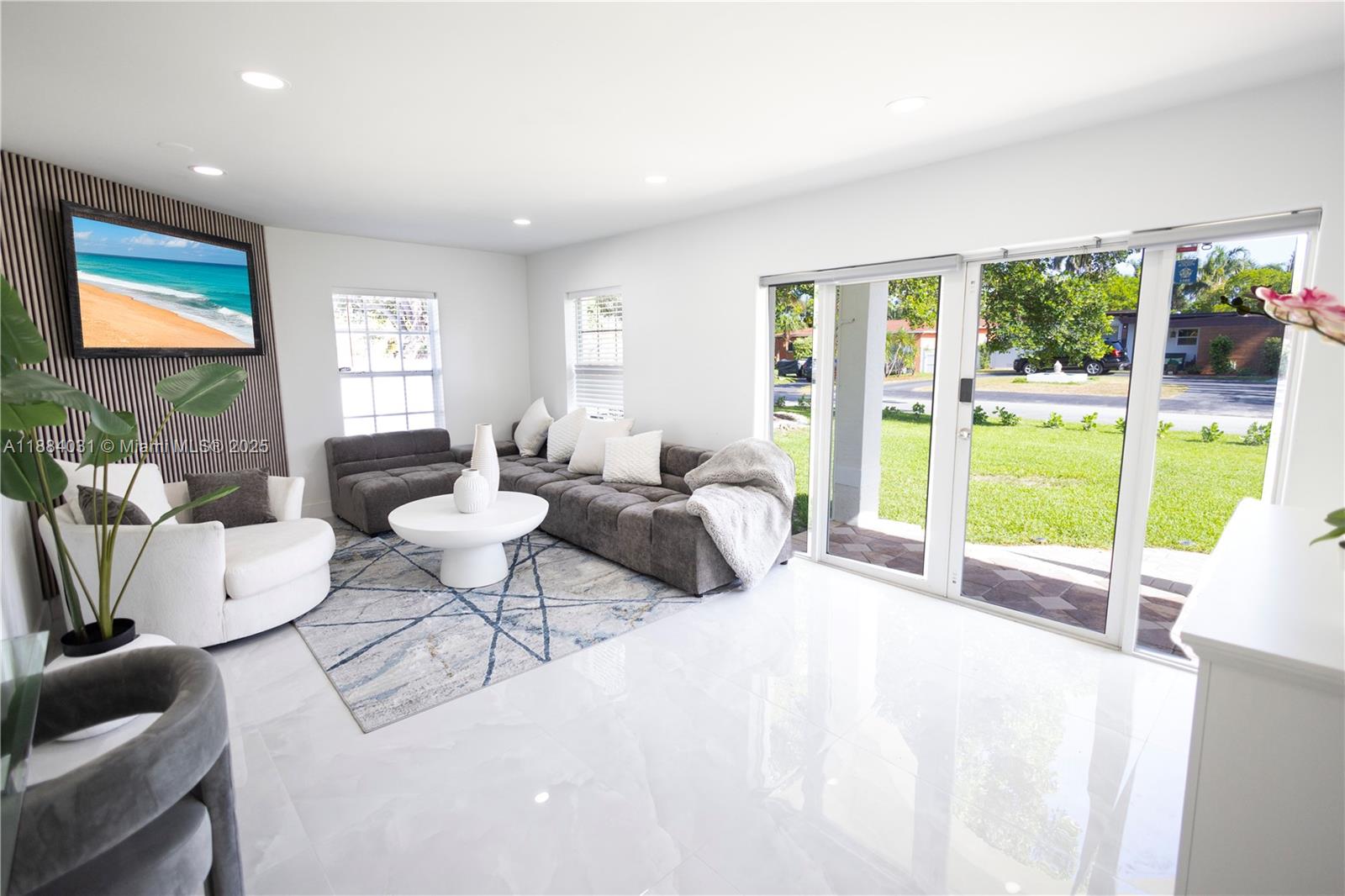 A living room features a grey sectional sofa, white armchair, and sliding glass patio doors — 1435 Grant St, Hollywood FL 33020, HOLLYWOOD, FL