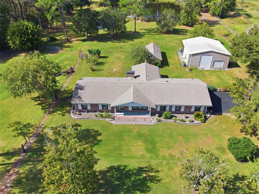 An aerial view shows a brick house with a large yard, detached garage, and pond — 9240 MOORE ROAD, LAKELAND, FL