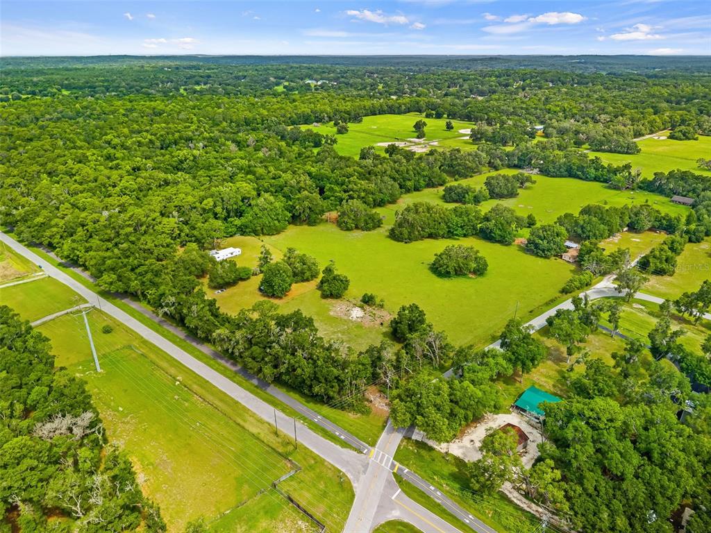 An aerial view shows a rural property with green pastures, scattered trees, and paved roads — 9287 WEATHERLY ROAD, BROOKSVILLE, FL