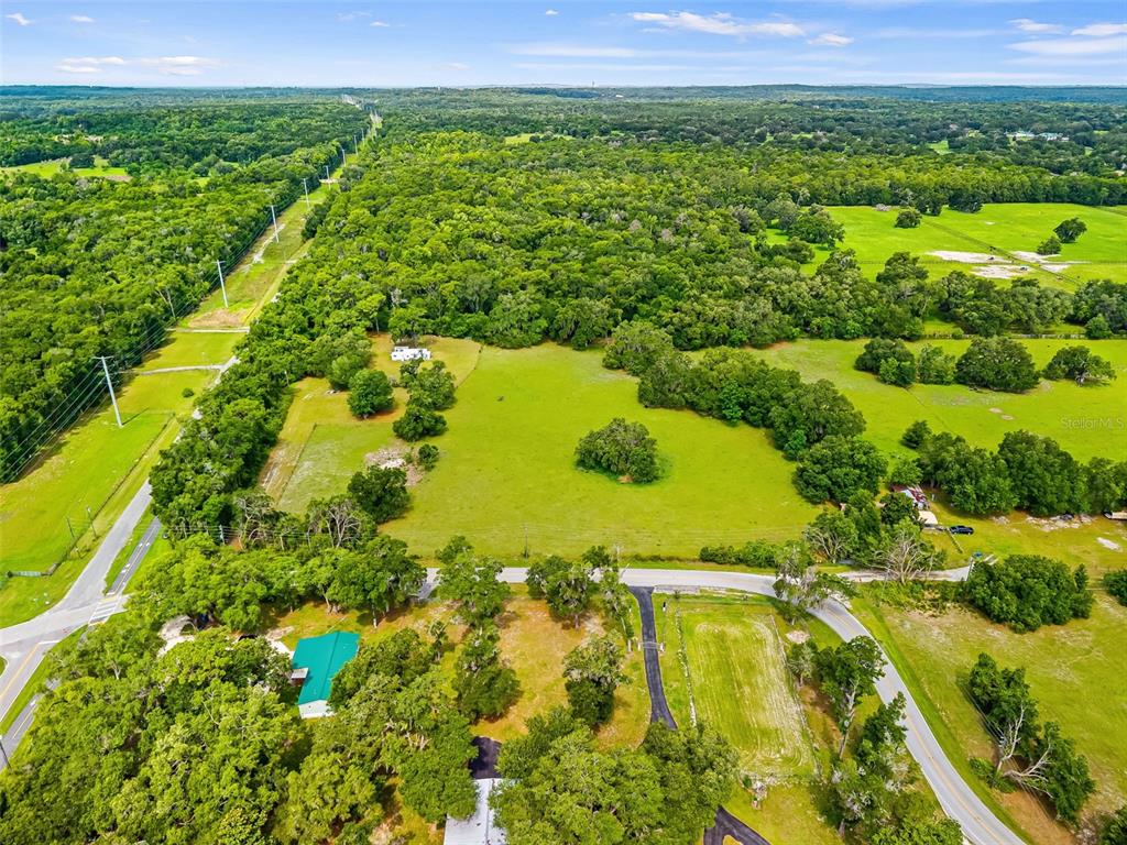 An aerial view shows a large, grassy pasture surrounded by dense trees and rural roads — 9287 WEATHERLY ROAD, BROOKSVILLE, FL