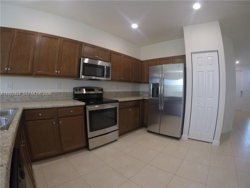 A kitchen features brown wooden cabinets, stainless steel appliances, and light-colored tile flooring — 25356 SW 116TH AVE, Miami FL 33032, MIAMI, FL