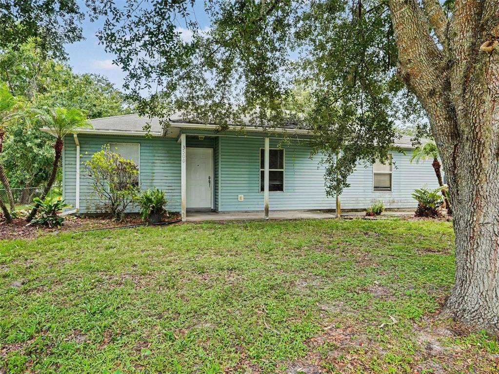 A light blue, single-story house with a front porch sits behind a large oak tree — 3500 SUZETTE DRIVE, KISSIMMEE, FL