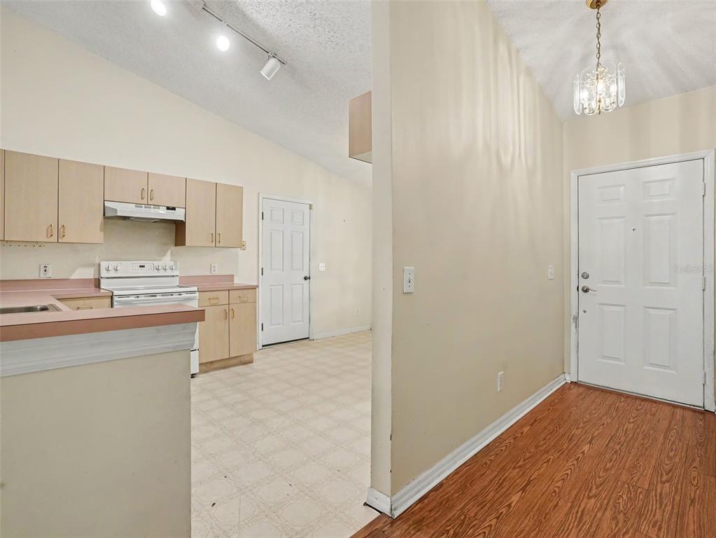 A kitchen with light wood cabinets and pink countertops sits adjacent to a wood-floored entryway — 3500 SUZETTE DRIVE, KISSIMMEE, FL