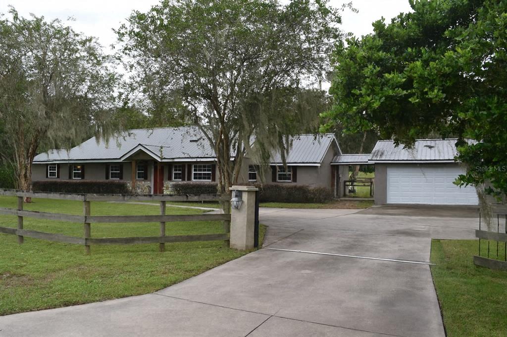 A single-story house with a metal roof, attached garage, and a wooden fence in front — 1722 NW 35 STREET, OCALA, FL