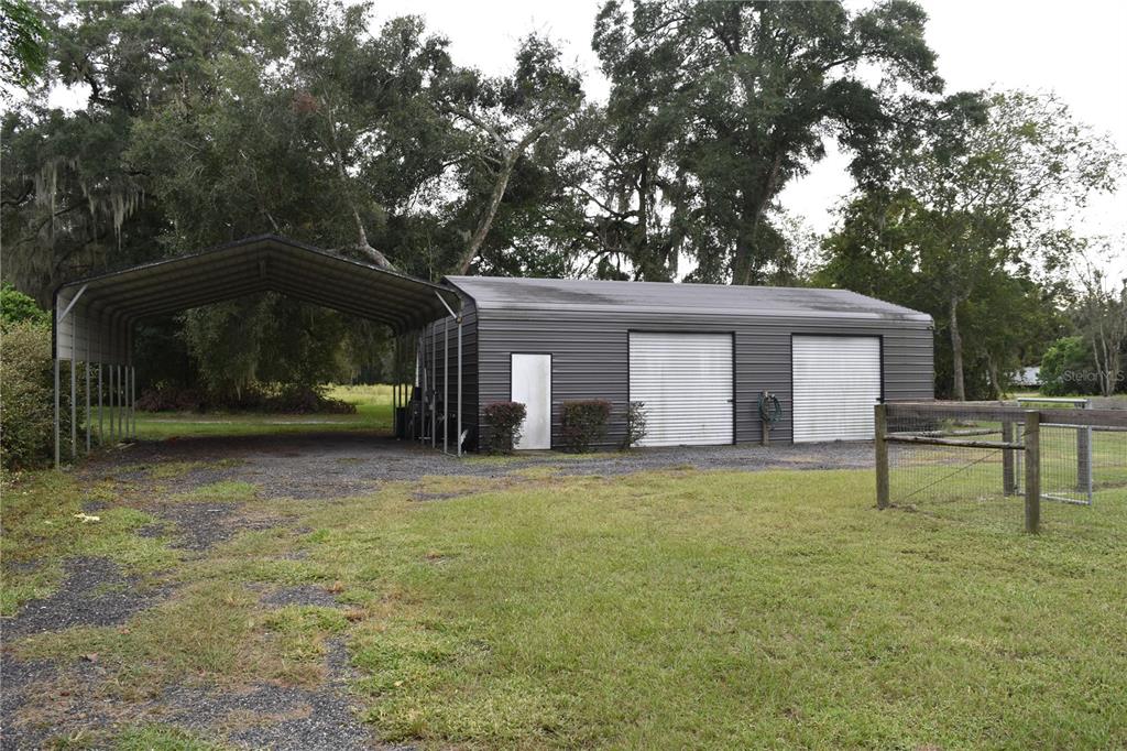 A dark metal workshop with two garage doors and an attached open-sided carport — 1722 NW 35 STREET, OCALA, FL