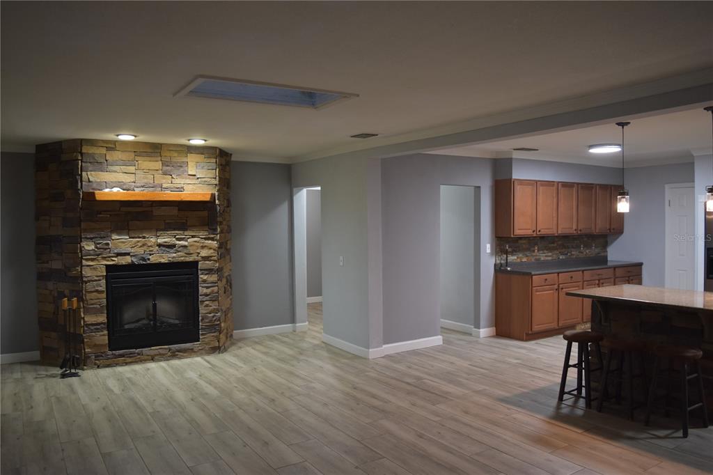 A living room with a stone fireplace and wood-look flooring opens into a kitchen area — 1722 NW 35 STREET, OCALA, FL