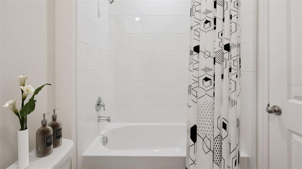A white tiled bathtub and shower combination features a patterned curtain and modern fixtures — 1348 FOUNTAIN VIEW STREET, ORMOND BEACH, FL