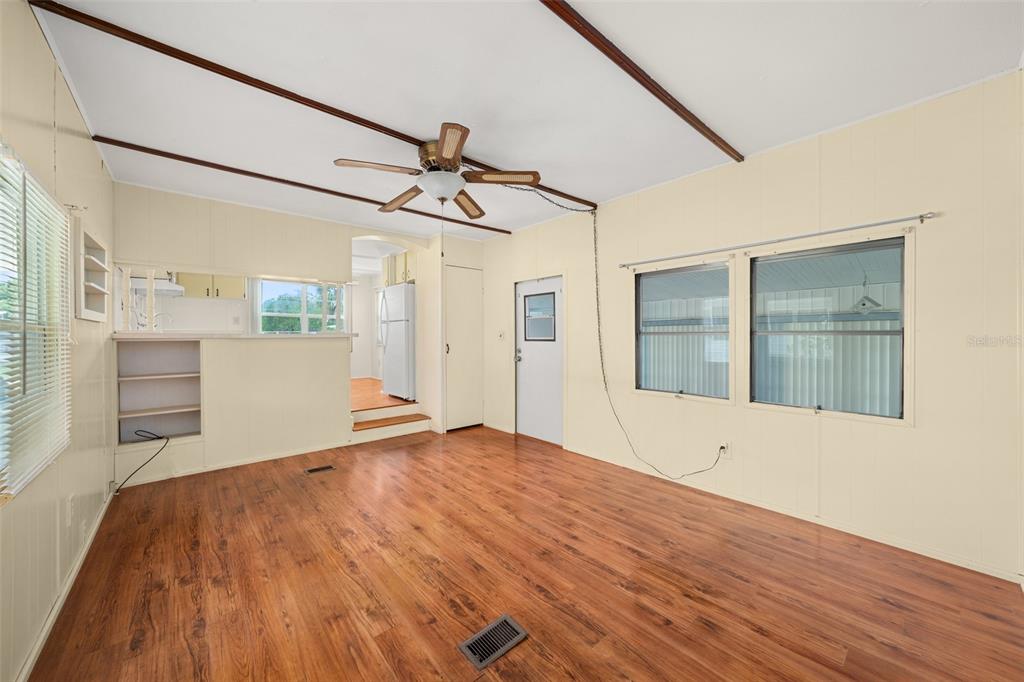 A living room with light yellow walls, wood-look flooring, a ceiling fan, and a kitchen — 3519 MAINE AVENUE, SEBRING, FL