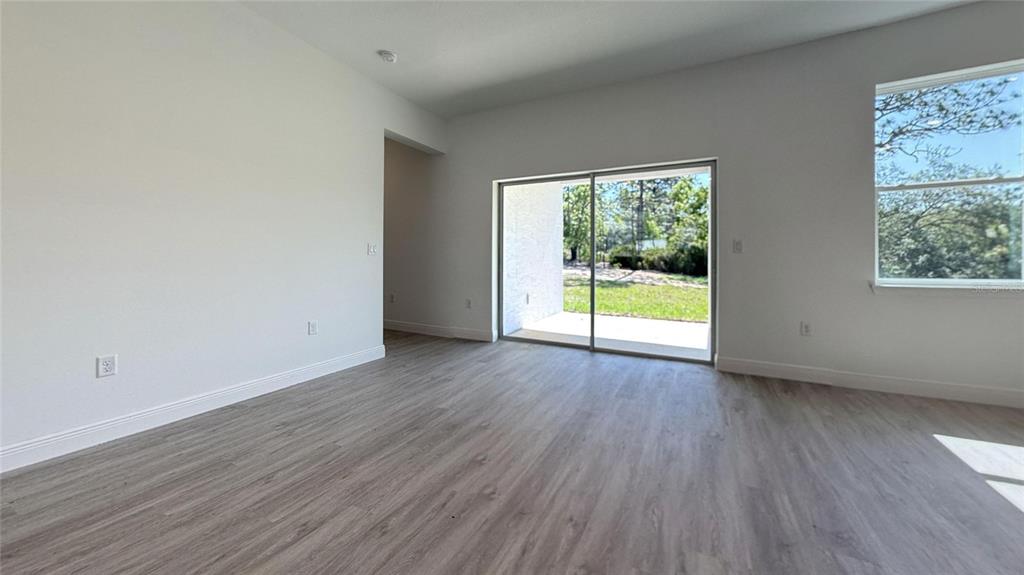 An empty room features light wood-look flooring, white walls, sliding glass doors, and a window — 6575 N GRAYTON TERRACE, CITRUS SPRINGS, FL