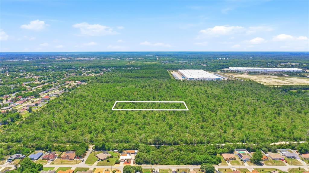 An aerial view shows a large, undeveloped wooded lot bordered by residential homes and warehouses — MCBRIDE AVENUE, DELTONA, FL