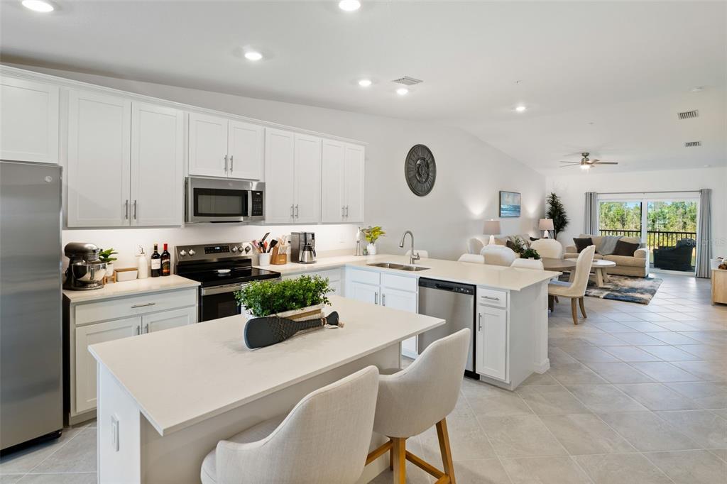 A modern kitchen with white cabinets, stainless steel appliances, and an island overlooks the living area — 14241 HERITAGE LANDING BOULEVARD UNIT 1827, PUNTA GORDA, FL