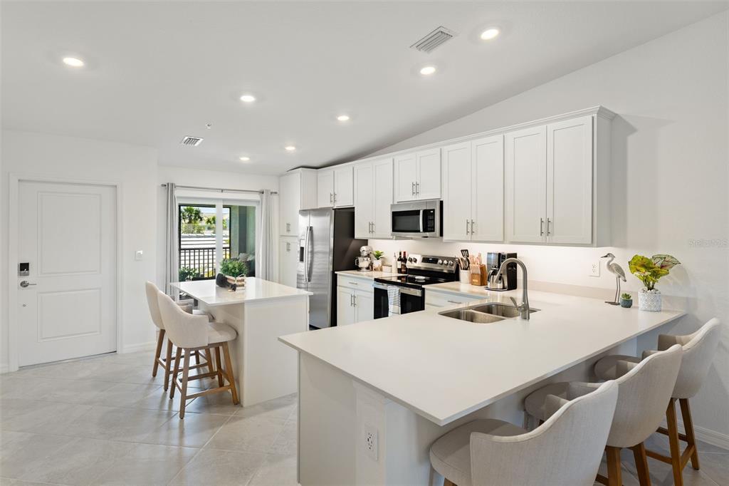 A modern kitchen features white cabinetry, quartz countertops, a center island, and stainless steel appliances — 14241 HERITAGE LANDING BOULEVARD UNIT 1827, PUNTA GORDA, FL