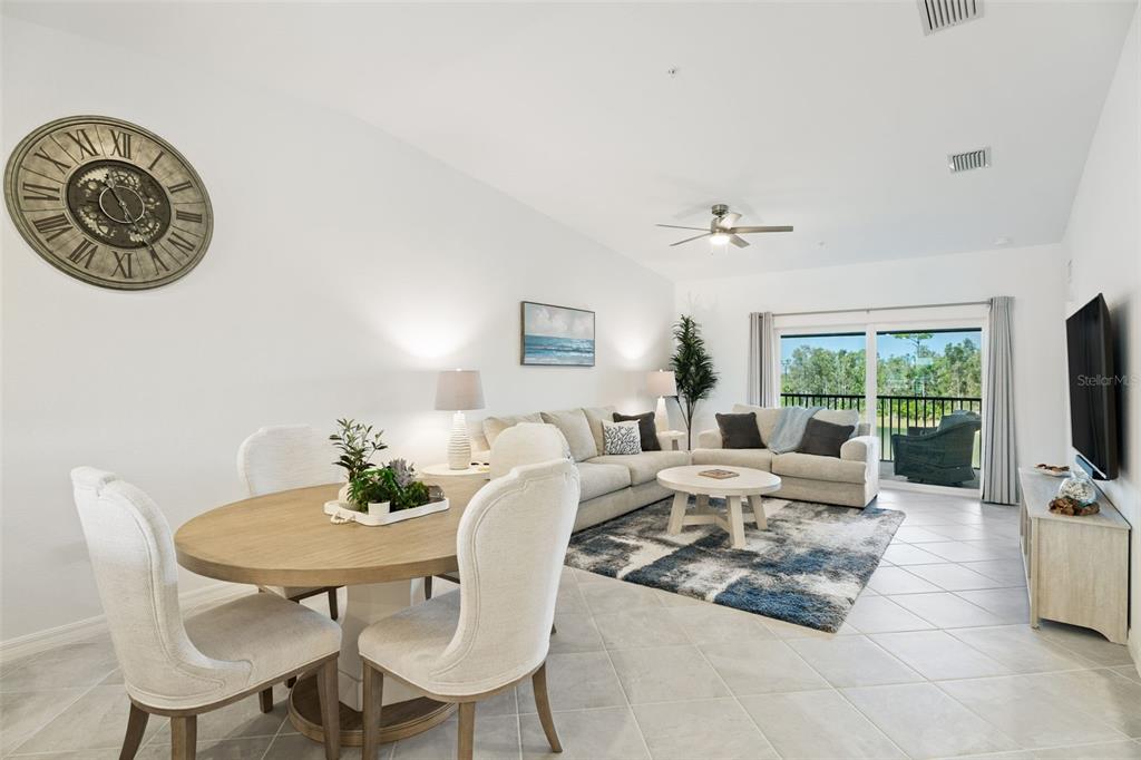 A living room and dining area with tile floors, neutral furniture, and a large wall clock — 14241 HERITAGE LANDING BOULEVARD UNIT 1827, PUNTA GORDA, FL