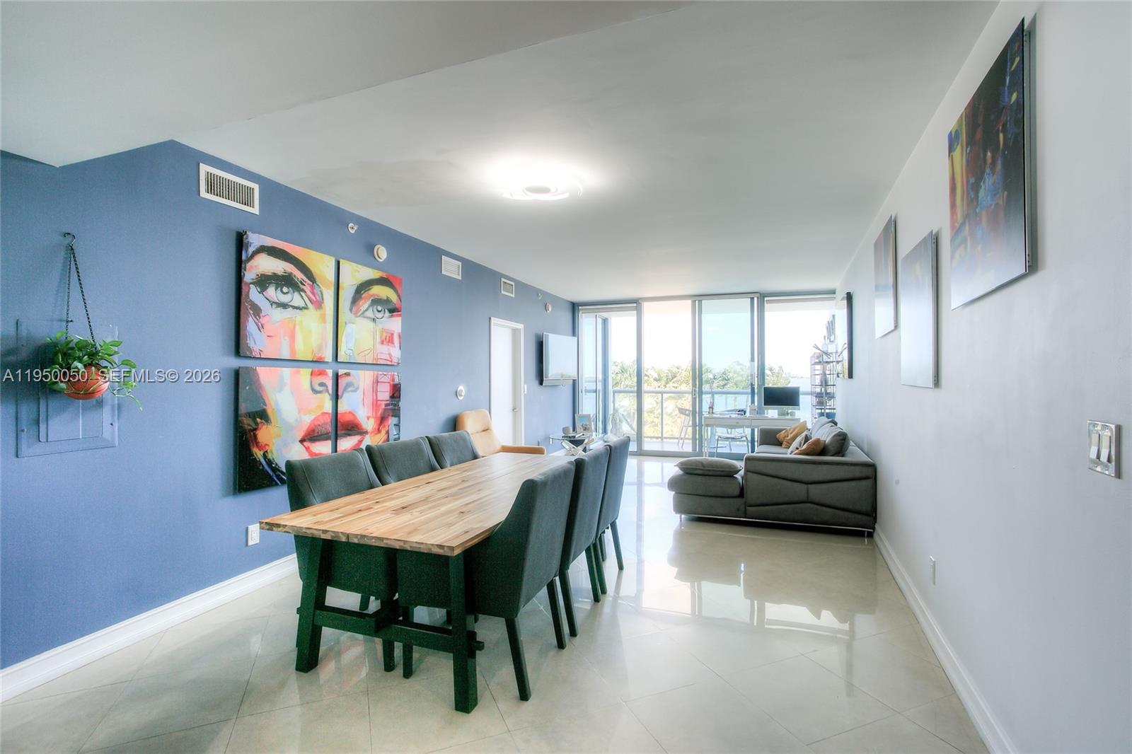 A dining area with a wooden table and blue chairs sits before a living room — 601 NE 36th St # 710, Miami FL 33137, MIAMI, FL