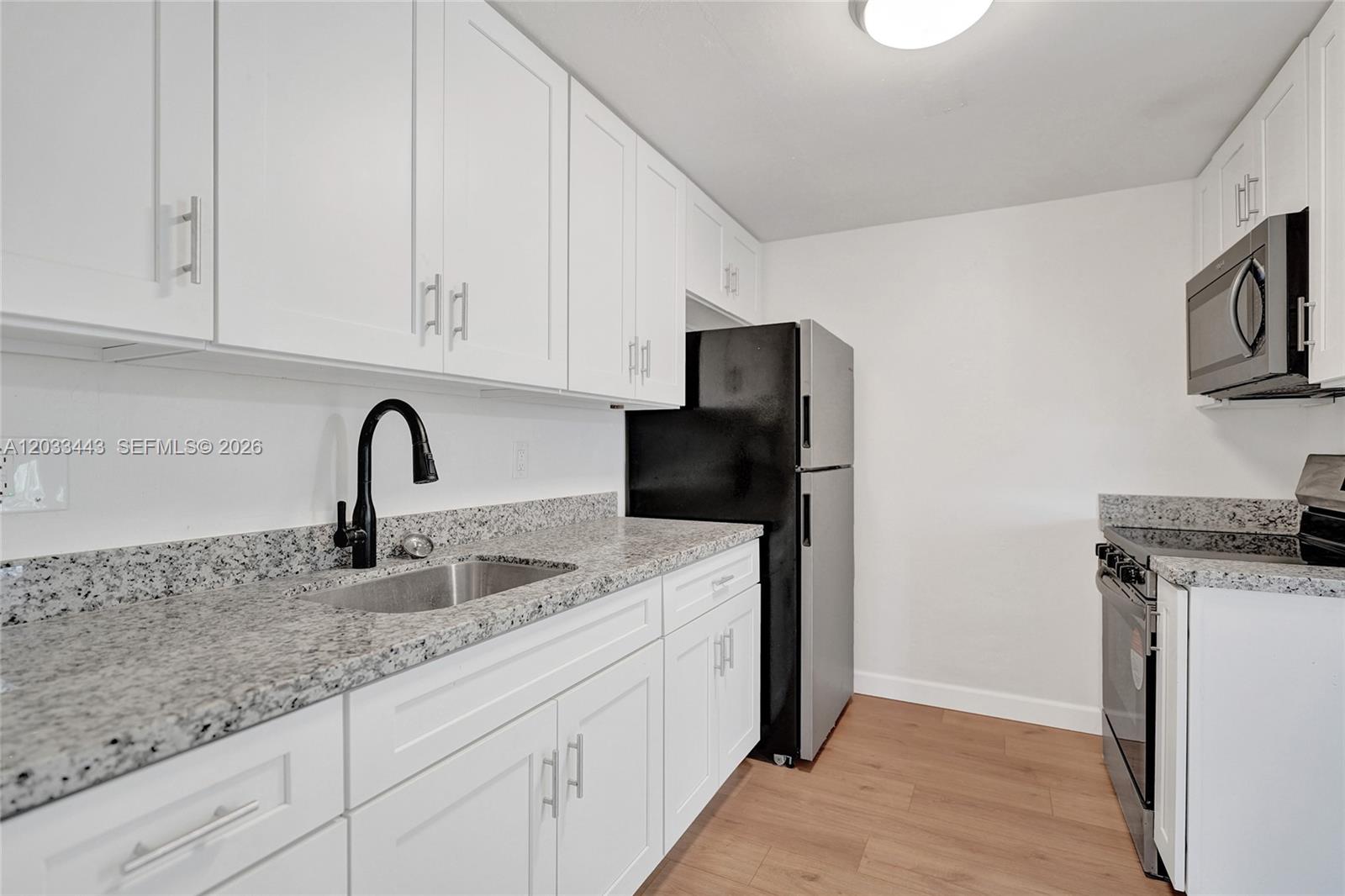 A kitchen features white cabinets, granite countertops, a black refrigerator, and a stainless steel sink — 307 NW 11th Ave, Delray Beach FL 33444, DELRAY BEACH, FL