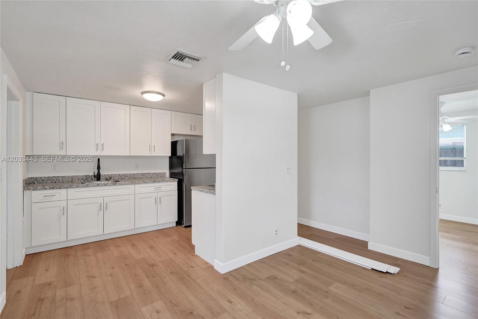 A kitchen with white cabinets, granite countertops, and wood-look flooring opens to a dining area — 307 NW 11th Ave, Delray Beach FL 33444, DELRAY BEACH, FL