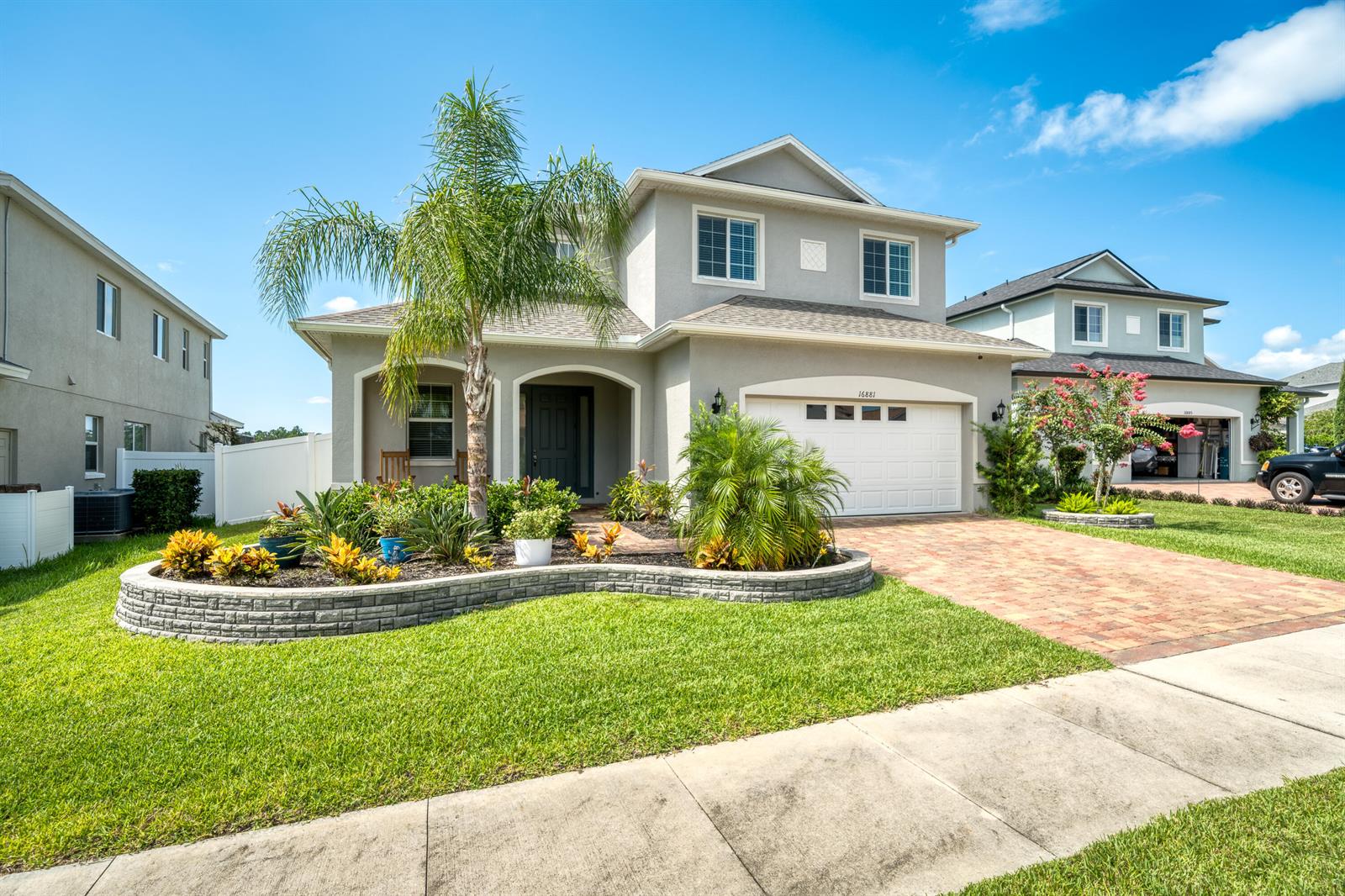 A two-story suburban house with a brick driveway, palm tree, and curved stone garden bed — 16881 Meadows Street, Clermont FL 34714, CLERMONT, FL
