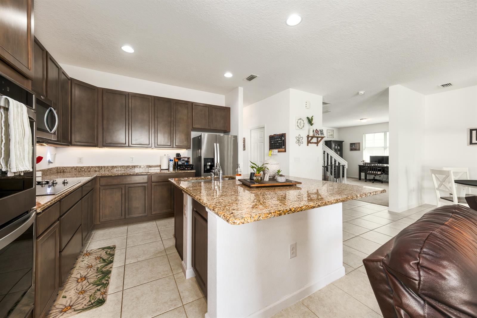 A kitchen features dark wood cabinets, granite countertops, a central island, and tile flooring — 16881 Meadows Street, Clermont FL 34714, CLERMONT, FL