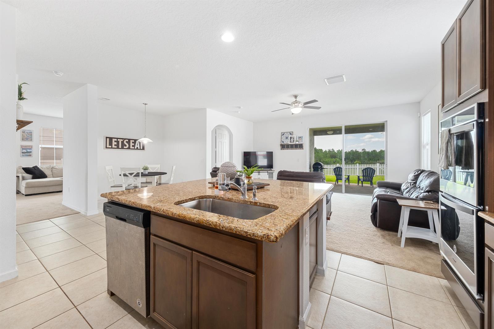 A kitchen island with a granite countertop and sink overlooks a living area and patio — 16881 Meadows Street, Clermont FL 34714, CLERMONT, FL