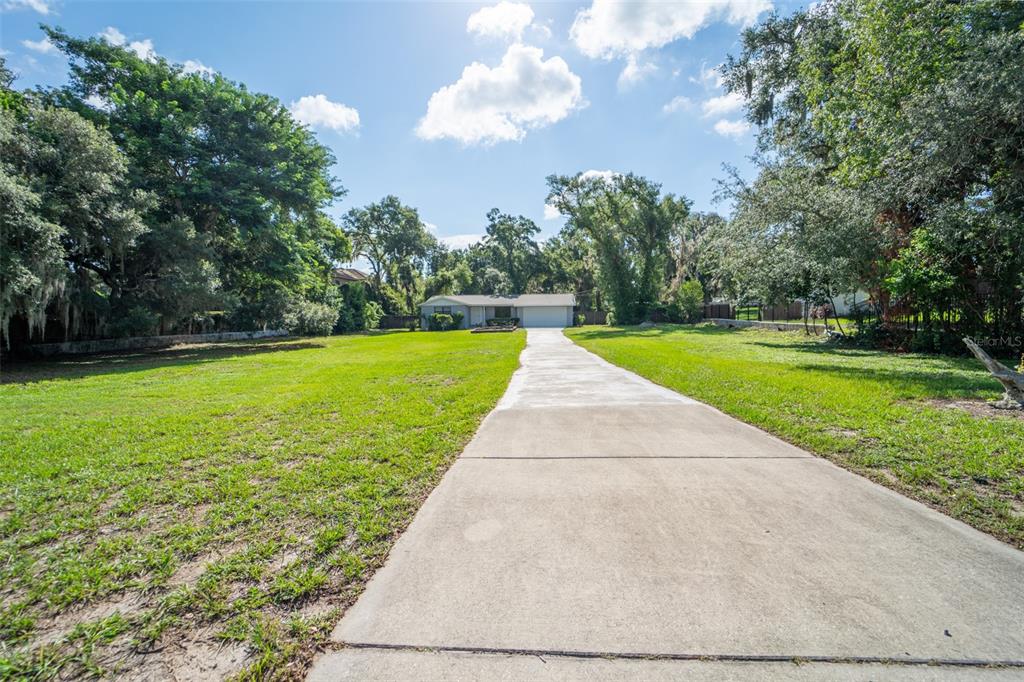 A long concrete driveway leads to a single-story house surrounded by large trees and grass — 8214 VALRIE LANE, RIVERVIEW, FL