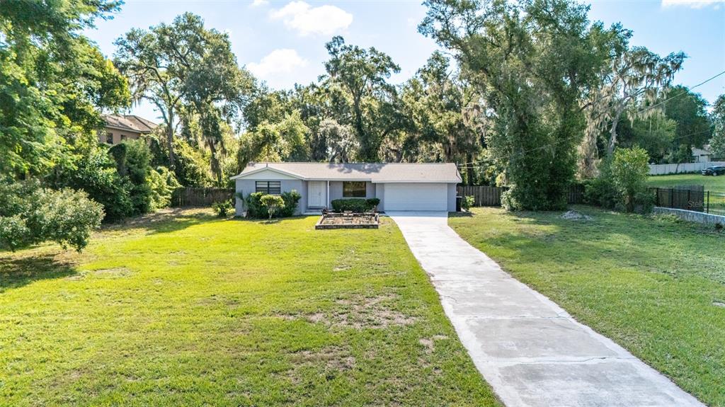 A single-story house with a concrete driveway sits on a large, grassy lot with trees — 8214 VALRIE LANE, RIVERVIEW, FL