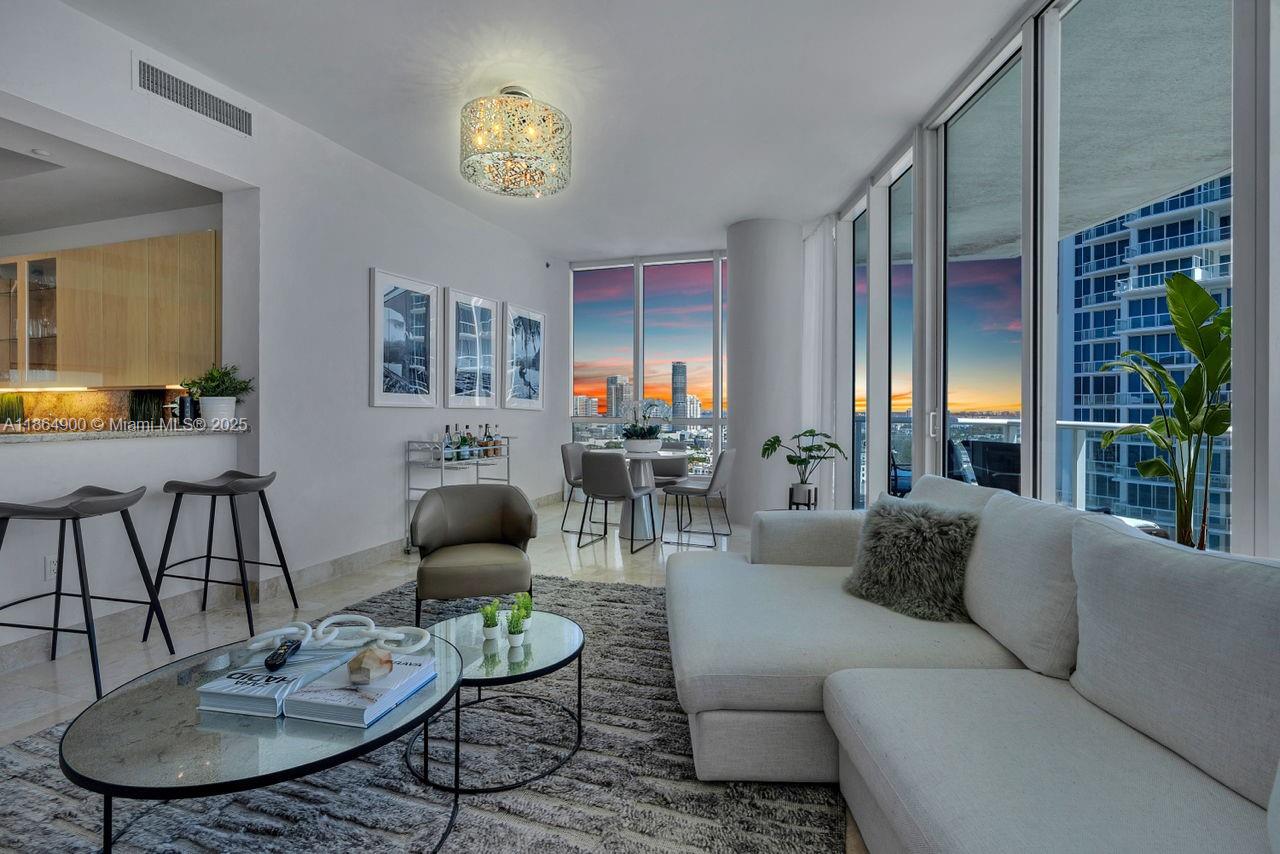 A modern living room features a white sectional sofa, glass coffee tables, and floor-to-ceiling windows — 100 S Pointe Dr # 2208, Miami Beach FL 33139, MIAMI BEACH, FL