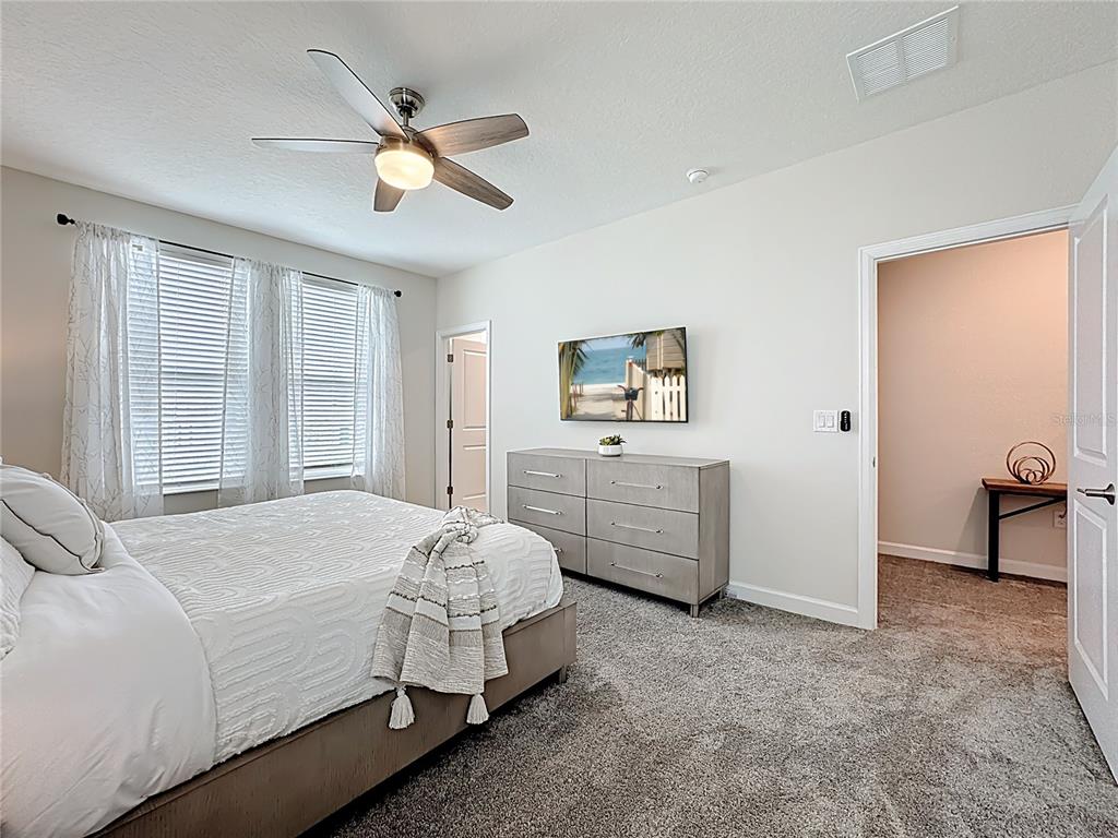 A bedroom features a gray upholstered bed, a ceiling fan, and neutral decor — 791 DROP SHOT DRIVE, DAVENPORT, FL