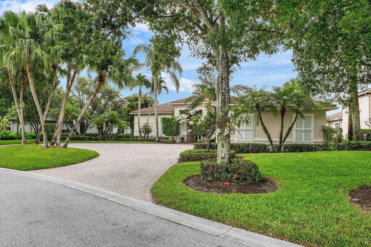 A single-story house with a paved driveway, lush landscaping, and palm trees under a blue sky — 118 W Village Way, Jupiter FL 33458, JUPITER, FL