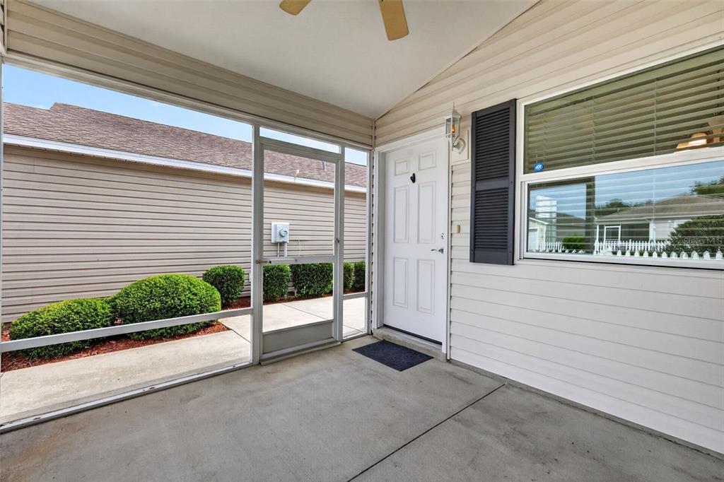 A covered concrete patio features a screened enclosure, a white door, and a window — 3419 CARRABELLE COURT, THE VILLAGES, FL