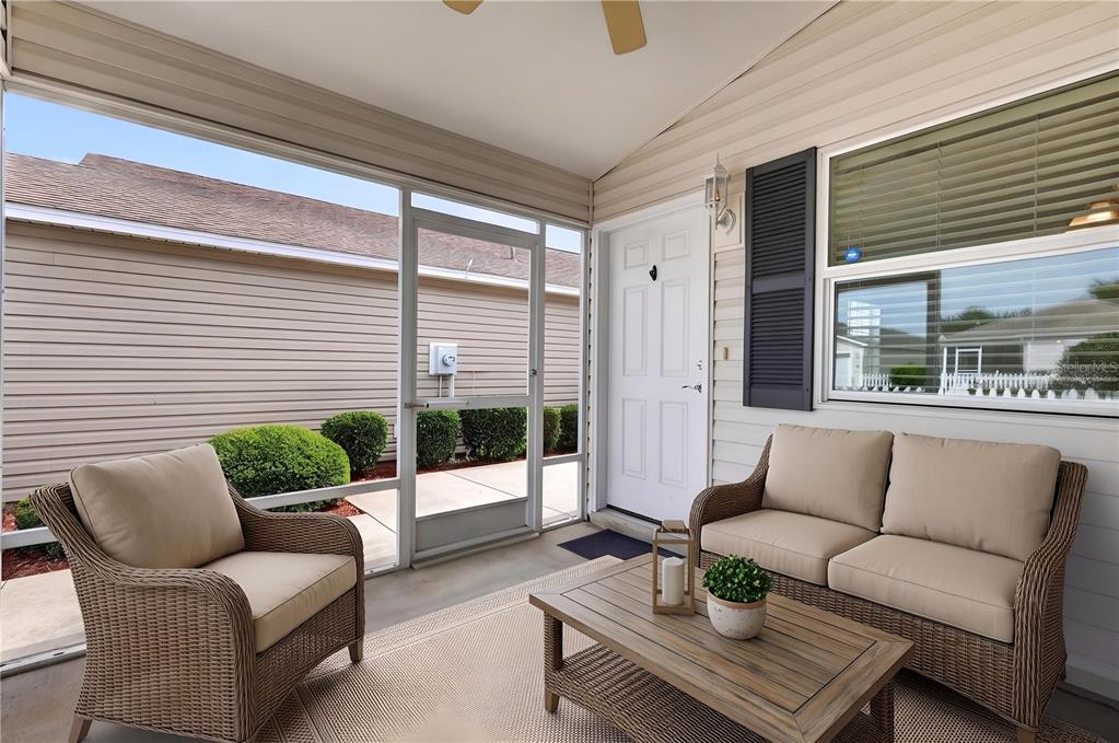 A screened-in patio features wicker furniture, a wooden coffee table, and a white entry door — 3419 CARRABELLE COURT, THE VILLAGES, FL