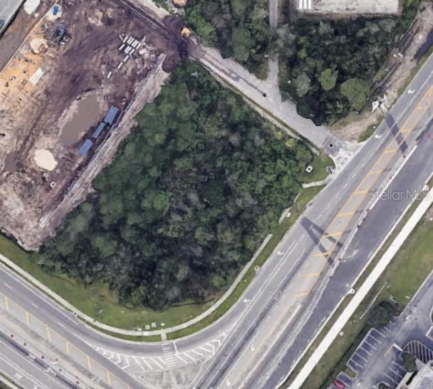 An aerial view shows a wooded, undeveloped rectangular lot situated between a road and construction site — E OSCEOLA PARKWAY, KISSIMMEE, FL