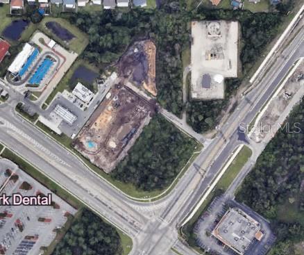 This aerial view shows a construction site located between a commercial parking lot and woods — E OSCEOLA PARKWAY, KISSIMMEE, FL