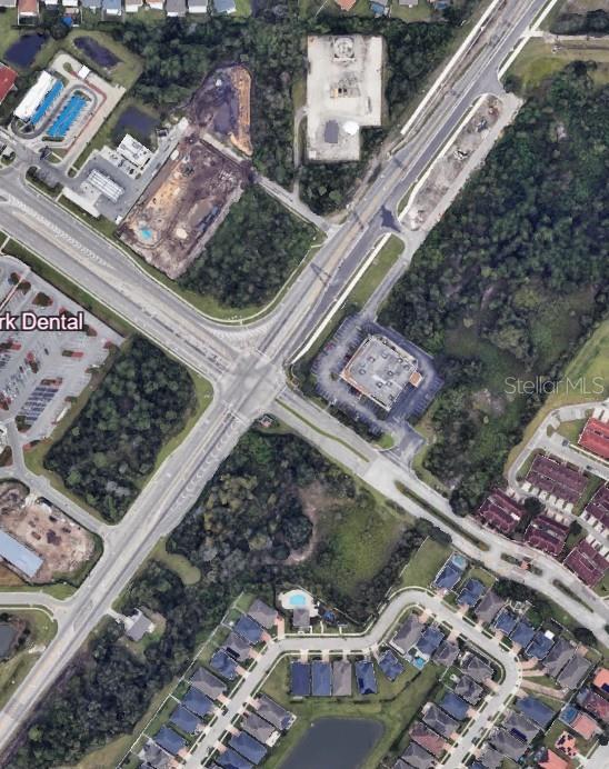 This aerial view shows a road intersection surrounded by commercial buildings, wooded areas, and residential neighborhoods — E OSCEOLA PARKWAY, KISSIMMEE, FL
