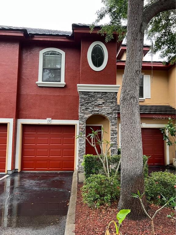 A red townhouse exterior features a stone-accented entryway, a garage, and an oval window — 2139 CHIANTI PLACE UNIT 5-0152, PALM HARBOR, FL
