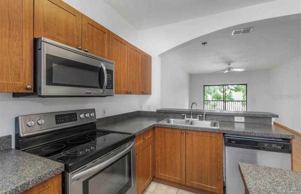 A kitchen with wood cabinets, stainless steel appliances, and a pass-through window to the living area — 2139 CHIANTI PLACE UNIT 5-0152, PALM HARBOR, FL