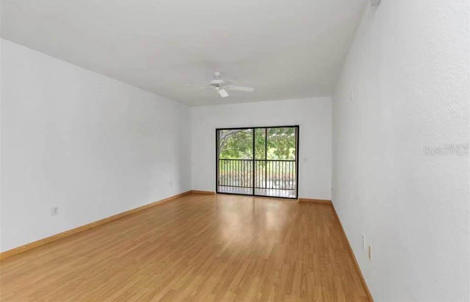 An empty room with light wood flooring, white walls, a ceiling fan, and sliding doors — 2139 CHIANTI PLACE UNIT 5-0152, PALM HARBOR, FL