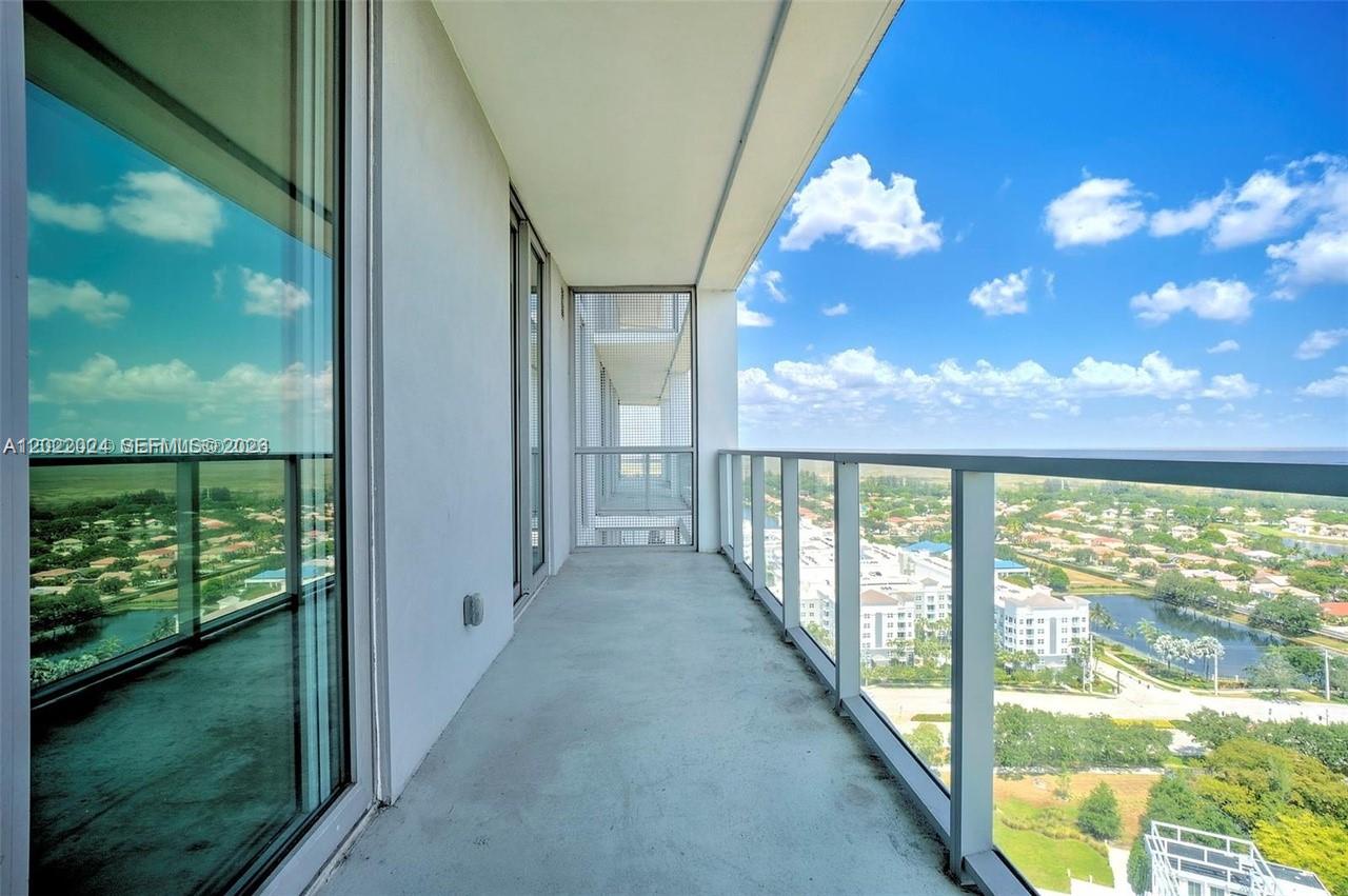 A high-rise balcony features a concrete floor, glass railings, and a view of suburban landscaping — 2000 Metropica Way # 2202, Sunrise FL 33323, SUNRISE, FL